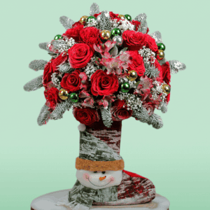 Christmas floral arrangement with festive red blooms, seasonal greenery, ornaments, and a wrapped Christmas present, beautifully designed for holiday celebrations and gifting.