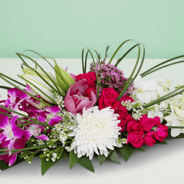 Purple, white and fuchsia long and low floral arrangement with fresh roses, orchids and seasonal blooms in an elegant table centerpiece design.