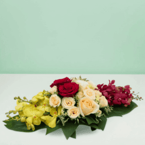 Long and low floral arrangement featuring red, yellow, and peach flowers with elegant seasonal blooms and lush greenery for table décor and special occasions.