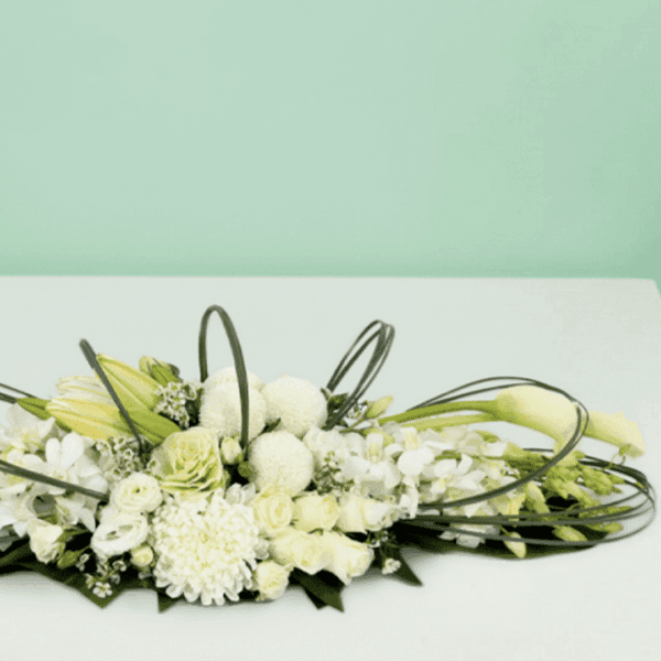 White long and low floral arrangement featuring elegant white roses, orchids, hydrangeas, and seasonal blooms in a modern centerpiece design for weddings, events, and luxury table décor.