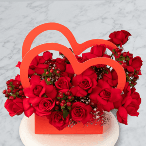 Red roses in a red box with two red paper heart accents.