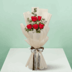 A bouquet of 5-stem red rose bouquet with soft greens wrapped in a White sheet