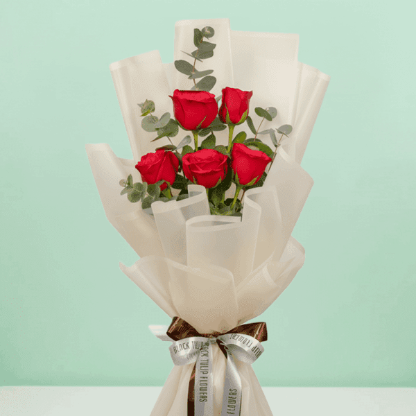 A bouquet of 5-stem red rose bouquet with soft greens wrapped in a White sheet