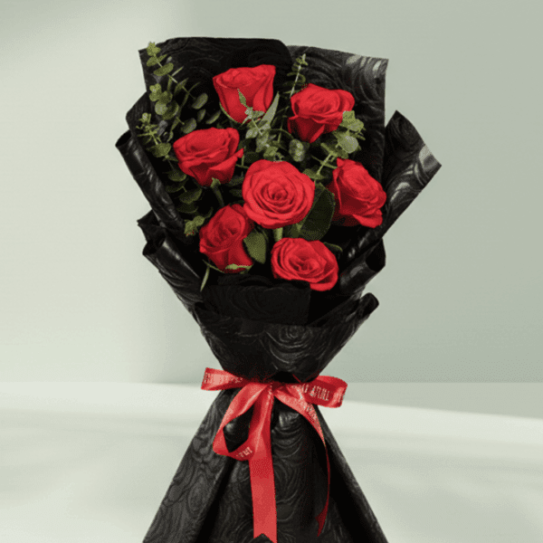A hand bouquet of 7 red roses, all tied together in a Black non woven paper with a red ribbon.
