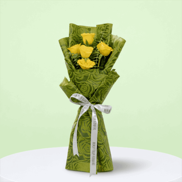 A Bouquet of 5 yellow roses bouquet with green wrap tied up in a pink ribbon
