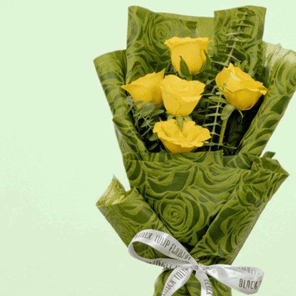 A Bouquet of 5 yellow roses bouquet with green wrap tied up in a pink ribbon
