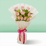 Pink roses wrapped in off-white, non-woven paper and tied with a vibrant pink satin ribbon with fresh green leaves.