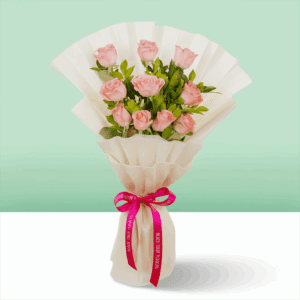 Pink roses wrapped in off-white, non-woven paper and tied with a vibrant pink satin ribbon with fresh green leaves.