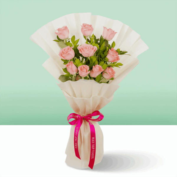 Pink roses wrapped in off-white, non-woven paper and tied with a vibrant pink satin ribbon with fresh green leaves.