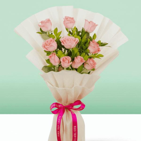 Pink roses wrapped in off-white, non-woven paper and tied with a vibrant pink satin ribbon with fresh green leaves.