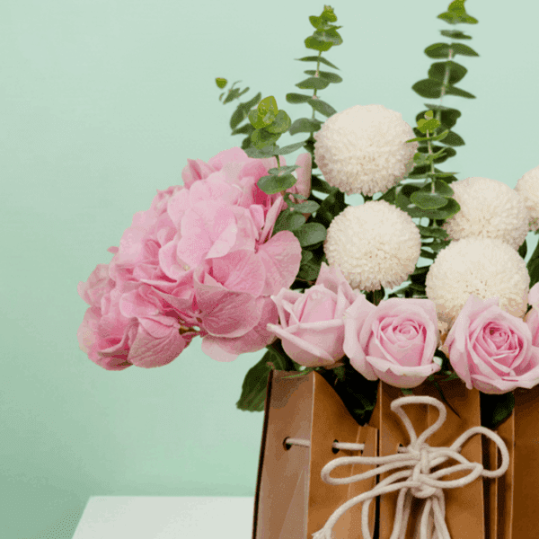 A soft-toned hydrangeas, ping pong blooms, and roses, gently arranged with eucalyptus leaves—all nestled in a chic, eco-friendly paper bag.