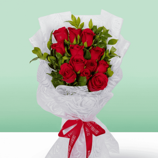 12 rich red roses with green leaves, wrapped in a white, textured non-woven paper and tied with a bright red ribbon.