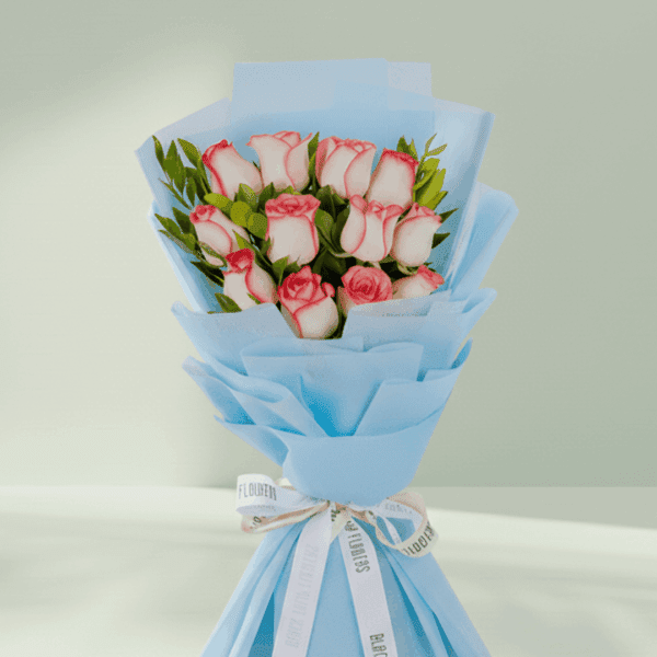 A bouquet of 12 white roses with green leaves, wrapped in bright fuchsia pink non-woven paper and tied with a white and black ribbon.