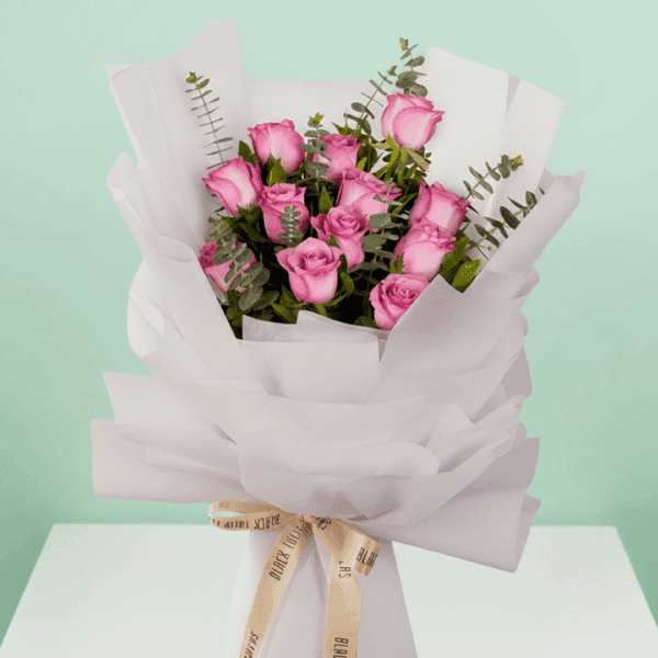 A bouquet of purple roses with green eucalyptus branches, wrapped in white non-woven paper and tied with a beige ribbon - 12 Roses Bouquet