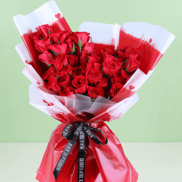 "Stunning red roses beautifully arranged with green leaves in Korean flower sheets, tied with a sleek black ribbon.