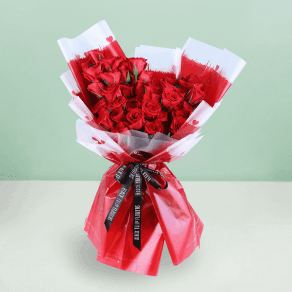 Stunning red roses beautifully arranged with green leaves in Korean flower sheets, tied with a sleek black ribbon.