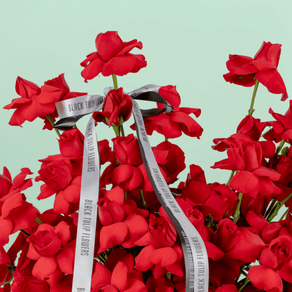 Round basket of 50 red roses arranged neatly with a white ribbon