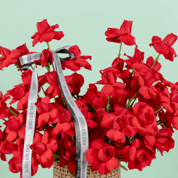 Round basket of 50 red roses arranged neatly with a white ribbon