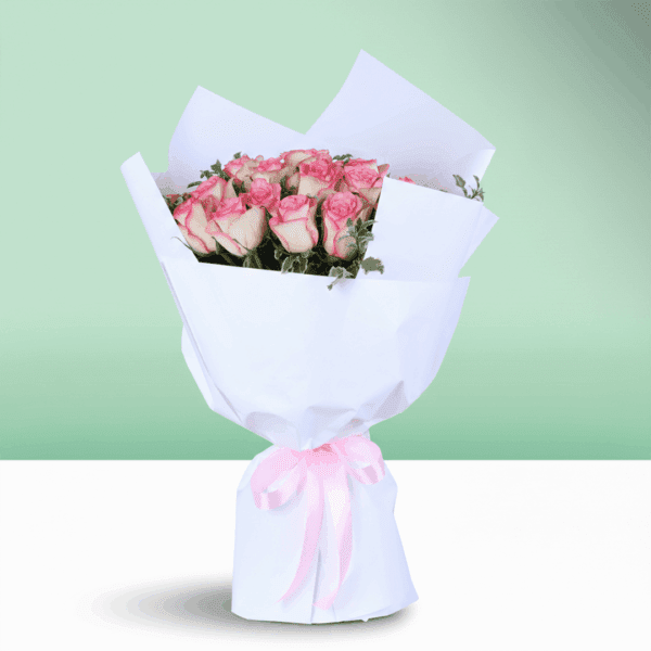 A blush pink roses bouquet wrapped in elegant white paper with greenery and pink ribbon.
