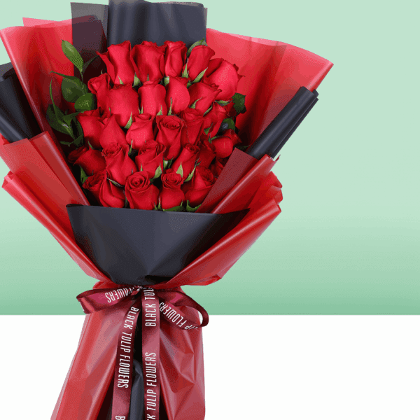 Fresh red roses arranged in a compact bouquet, wrapped in a black and red sheet and tied with a red ribbon