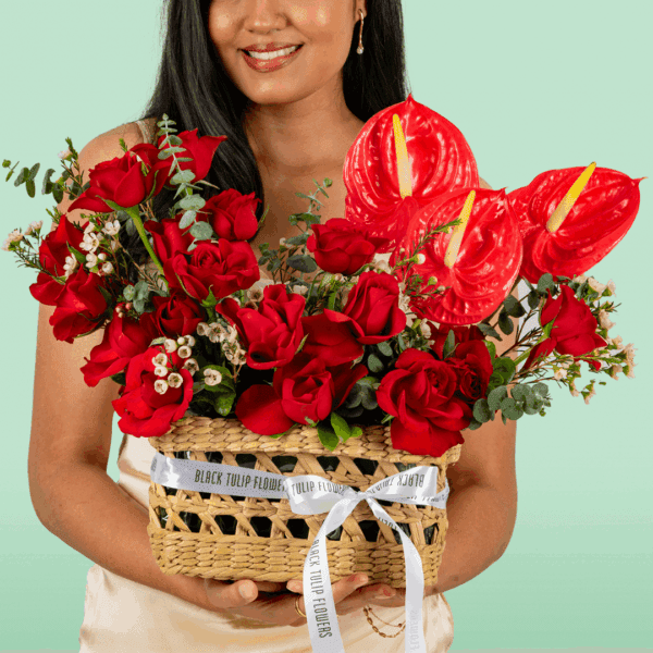A beautifully arranged rectangle basket featuring 25–30 vibrant red roses, complemented by exotic red Anthurium and delicate Waxflower stems