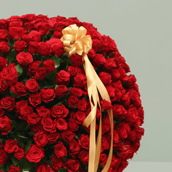 An overflowing arrangement of red roses in a white wicker basket, finished with a gold ribbon.