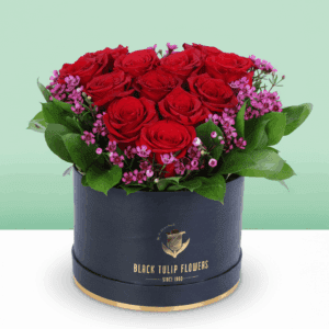 A black box featuring red roses in heart shape with purple filler flowers and green foliage.