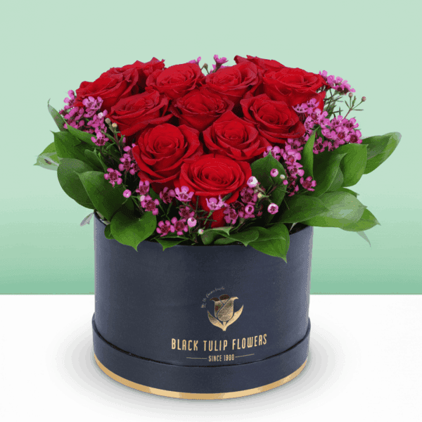 red-roses-purple-fillers-box (1) A black box featuring red roses in heart shape with purple filler flowers and green foliage.