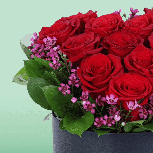red-roses-purple-fillers-box (4) A black box featuring red roses in heart shape with purple filler flowers and green foliage.