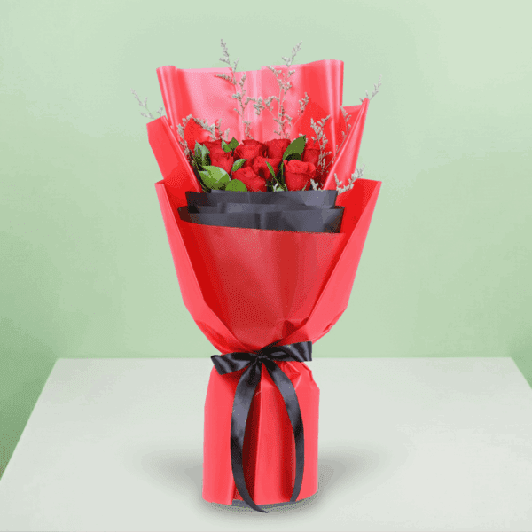 A bouquet of red roses with green foliage and delicate filler stems, wrapped in red and black, finished with a black ribbon.