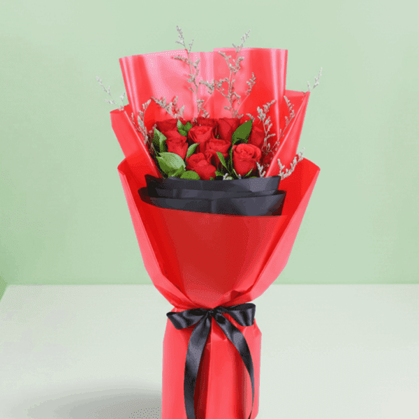 A bouquet of red roses with green foliage and delicate filler stems, wrapped in red and black, finished with a black ribbon.