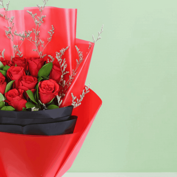 A bouquet of red roses with green foliage and delicate filler stems, wrapped in red and black, finished with a black ribbon.