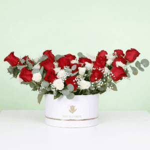 A white round flower box filled with red roses, white spray roses, baby’s breath, and eucalyptus.