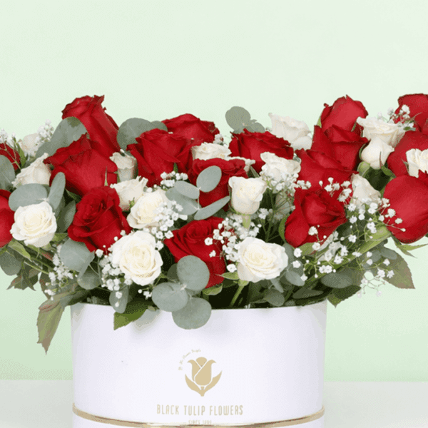 A white round flower box filled with red roses, white spray roses, baby’s breath, and eucalyptus.