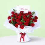Red hand-tied rose bouquet placed on a white table with soft fabric wrap and a message note