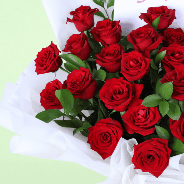 Red hand-tied rose bouquet placed on a white table with soft fabric wrap and a message note