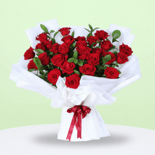 Red hand-tied rose bouquet placed on a white table with soft fabric wrap and a message note