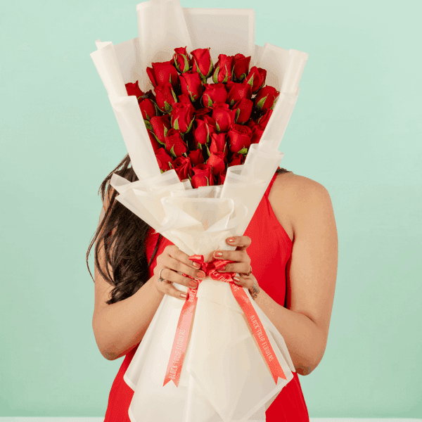 Woman in a red dress holding a Valentine’s bouquet of 30 fresh red roses, wrapped in elegant Korean-style flower sheets and finished with a red satin ribbon.