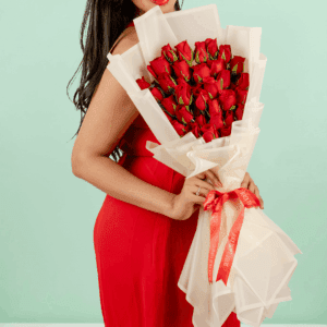 Woman in a red dress holding a Valentine’s bouquet of 30 fresh red roses, wrapped in elegant Korean-style flower sheets and finished with a red satin ribbon.