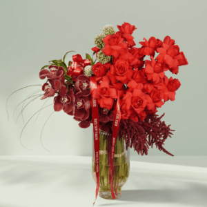 Luxury rose and cymbidium flower arrangement with red roses, cymbidium orchids, allium, and amaranthus displayed in a clear glass vase.