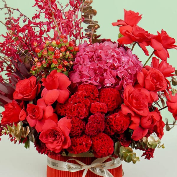 Designer red round box featuring vibrant red roses, hydrangeas, orchids, celosia, and eucalyptus, crafted for elegant gifting and celebrations.