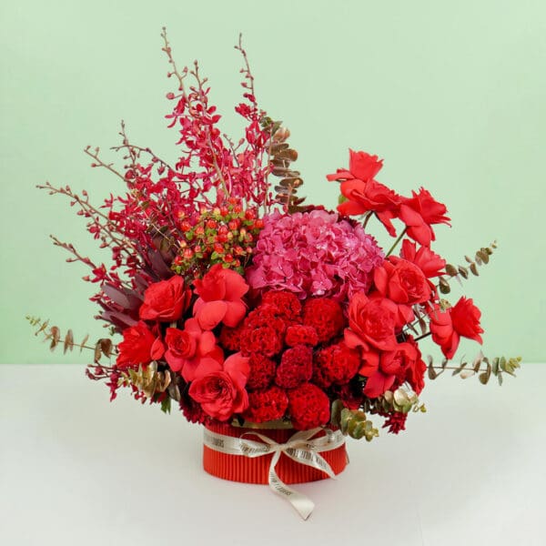 Designer red round box featuring vibrant red roses, hydrangeas, orchids, celosia, and eucalyptus, crafted for elegant gifting and celebrations.