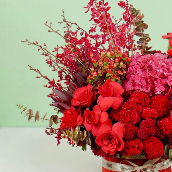 Designer red round box featuring vibrant red roses, hydrangeas, orchids, celosia, and eucalyptus, crafted for elegant gifting and celebrations.