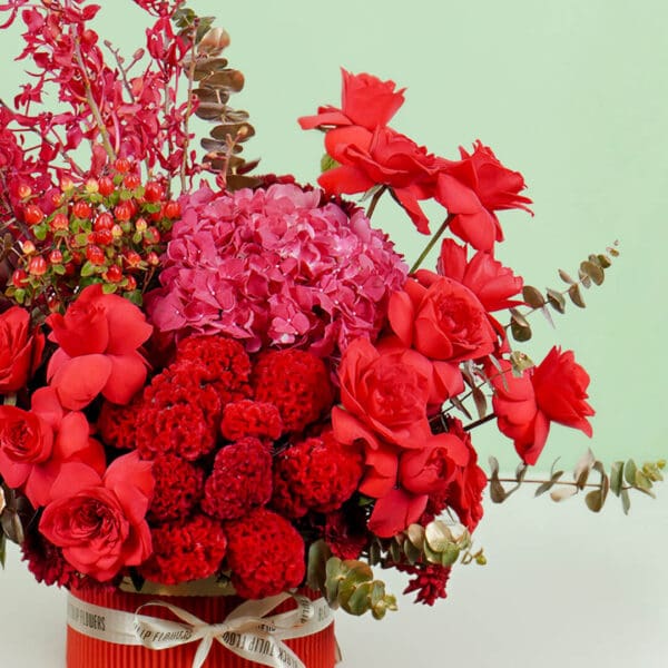 Designer red round box featuring vibrant red roses, hydrangeas, orchids, celosia, and eucalyptus, crafted for elegant gifting and celebrations.