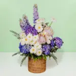 Grand flower basket arrangement with protea, hydrangea, delphinium, ping pong blooms, gerberas, and eucalyptus in a round basket.