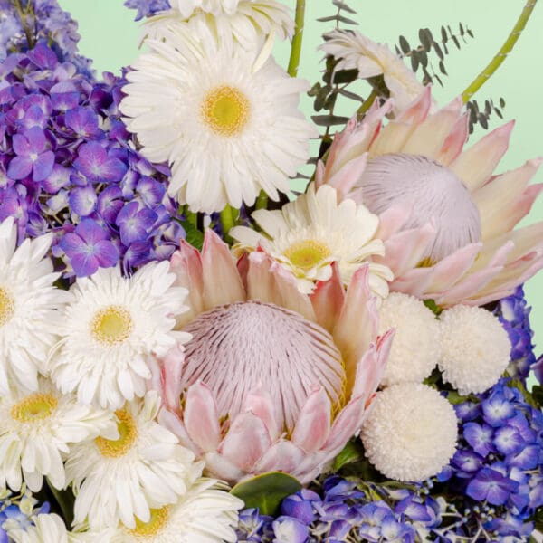 Grand flower basket arrangement with protea, hydrangea, delphinium, ping pong blooms, gerberas, and eucalyptus in a round basket.