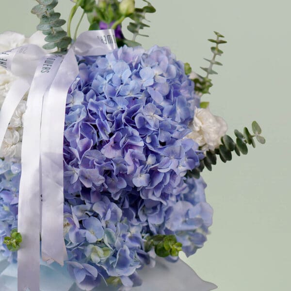 Grand bouquet of mixed seasonal flowers featuring roses, hydrangeas, cymbidium, and eustoma in an elegant round vase.