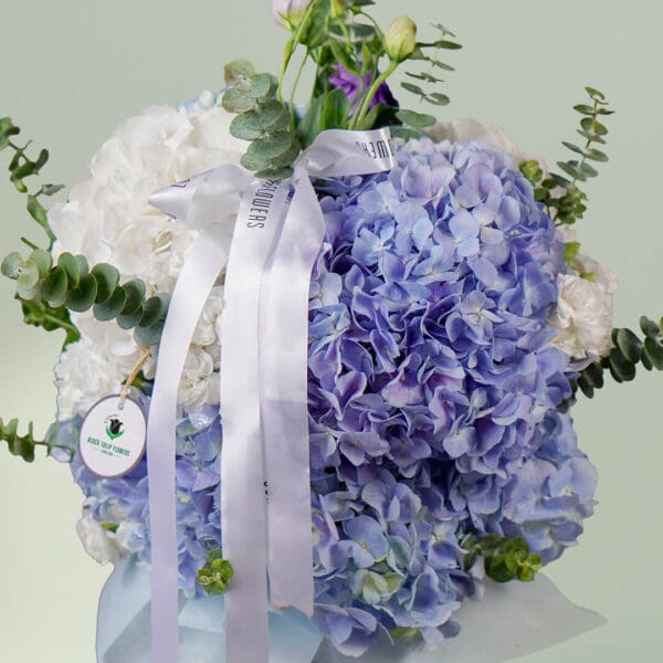 Grand bouquet of mixed seasonal flowers featuring roses, hydrangeas, cymbidium, and eustoma in an elegant round vase.